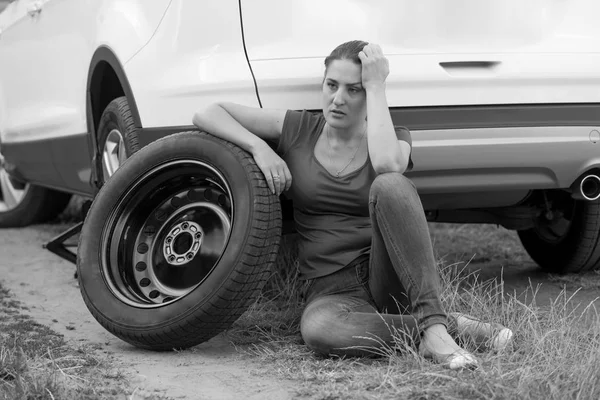 Retrato en blanco y negro de la joven disgustada inclinada rueda de repuesto del coche y la espera de servicio automático — Foto de Stock