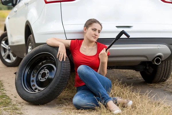 Triste giovane donna seduta a rotto auto e tenendo chiave inglese — Foto Stock