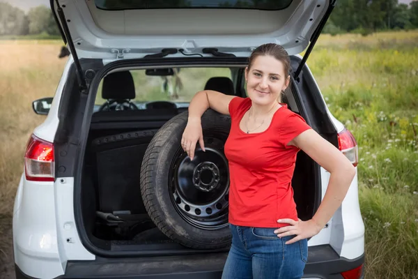 Portrait of young woman leaning on car spare wheel in field — Stock Photo, Image