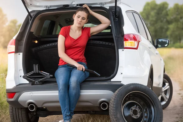 Mujer joven molesta sentada en el maletero de un coche abierto en la carretera desierta en el campo y esperando ayuda —  Fotos de Stock