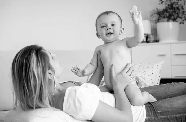Foto en blanco y negro del alegre niño sonriente sentado en la madre acostado en la cama — Foto de Stock
