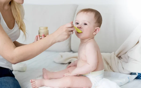 Genç anne oturma odasında kanepede bez bebek oğlu besleme — Stok fotoğraf