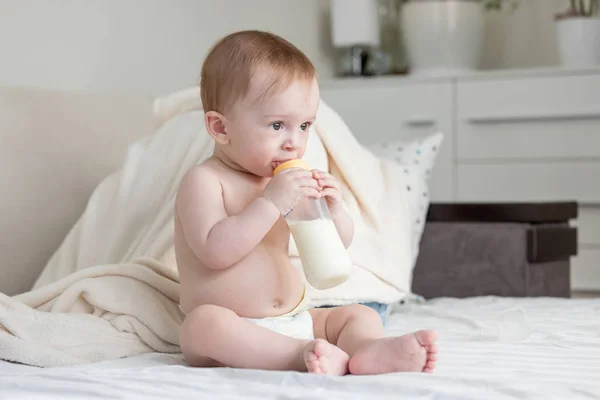 Şirin bebek çocuk yatağa oturmuş ve süt Şişeden içme bezli portresi — Stok fotoğraf