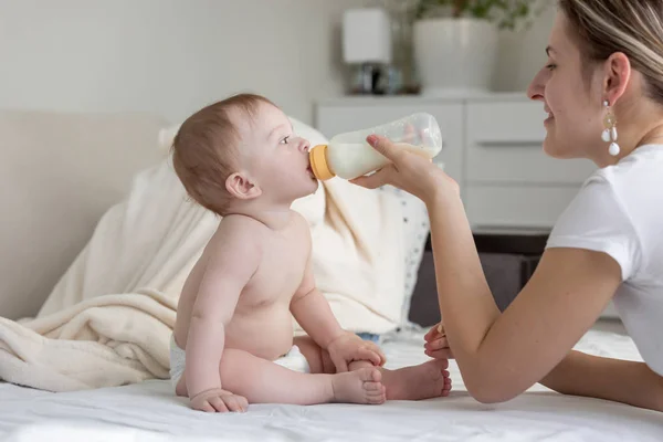 Gyönyörű fiatal nő, amely a tej a baba fia ül ágyas — Stock Fotó