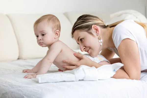 Retrato de una hermosa joven acariciando y mirando a su hijo bebé acostado en la cama —  Fotos de Stock