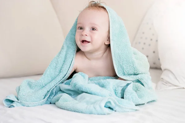 Porträt des niedlichen Jungen, der auf dem Bett liegt, bedeckt mit einem großen Handtuch — Stockfoto