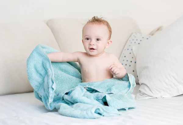 Bonito 9 meses de idade menino coberto de toalha azul sentado na cama após o banho — Fotografia de Stock