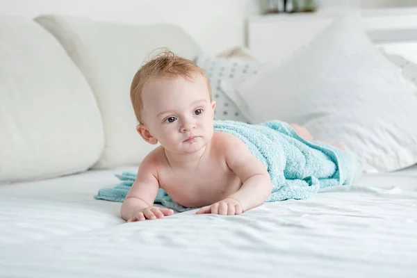 Adorable bébé garçon de 9 mois couché sur le lit sous une grande serviette bleue après avoir pris un bain — Photo