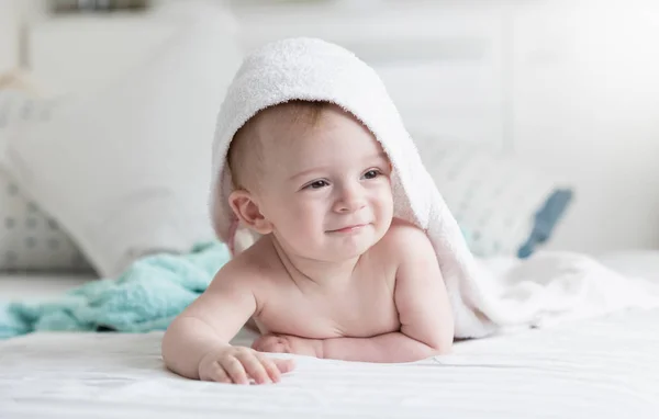 Portrait of beautiful smiling baby boy in white towel lying on bed — Stock Photo, Image