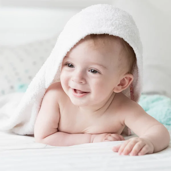 Nahaufnahme Porträt eines lächelnden Jungen, der nach dem Duschen mit einem Handtuch auf dem Kopf im Bett liegt — Stockfoto