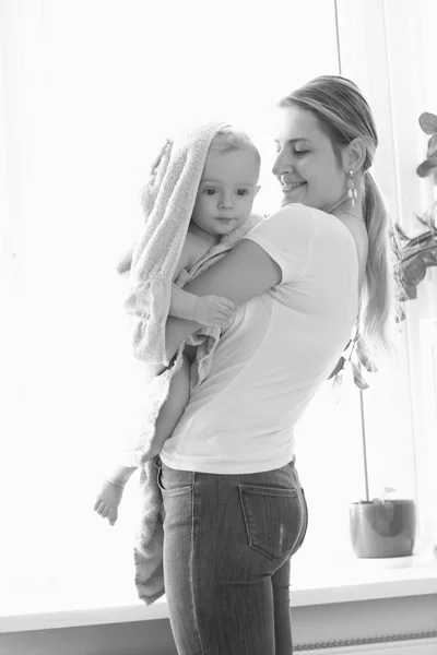 Black and white photo of young mother holding her baby covred in big white towel — Stock Photo, Image