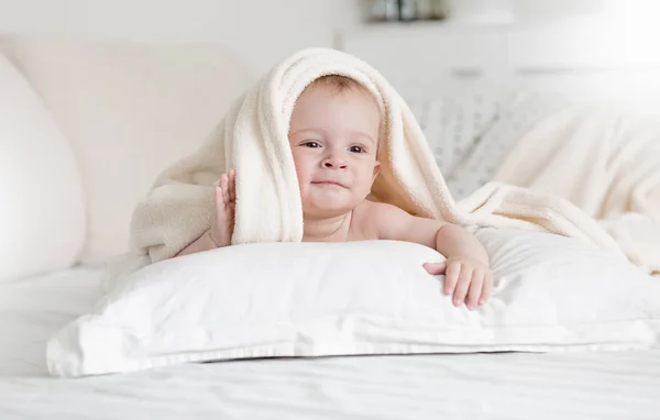 Porträtt av bedårande 9 månader gammal pojke liggande på sängen under stora mjuk filt — Stockfoto