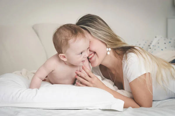 Toned portrait of laughing young mother with her 9 months old baby son on bed in bedroom — Stock Photo, Image