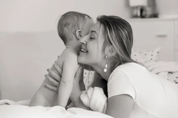 Black and white portrait of young caring mother hugging her baby son sitting on bed — Stock Photo, Image