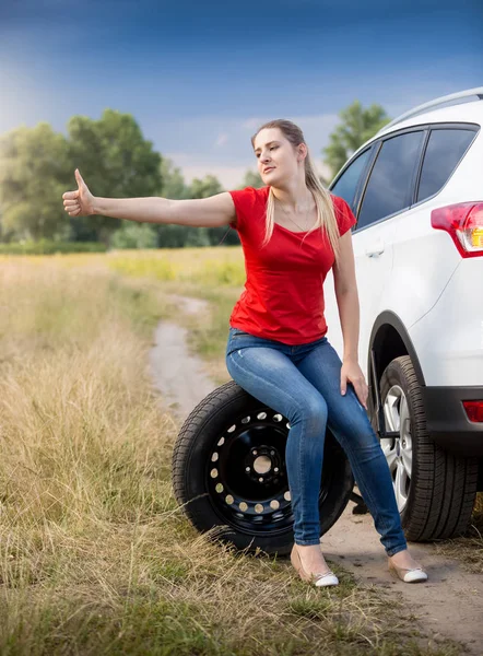 Young woman sitting at her broken car in field and hitch-hiking Stock Picture
