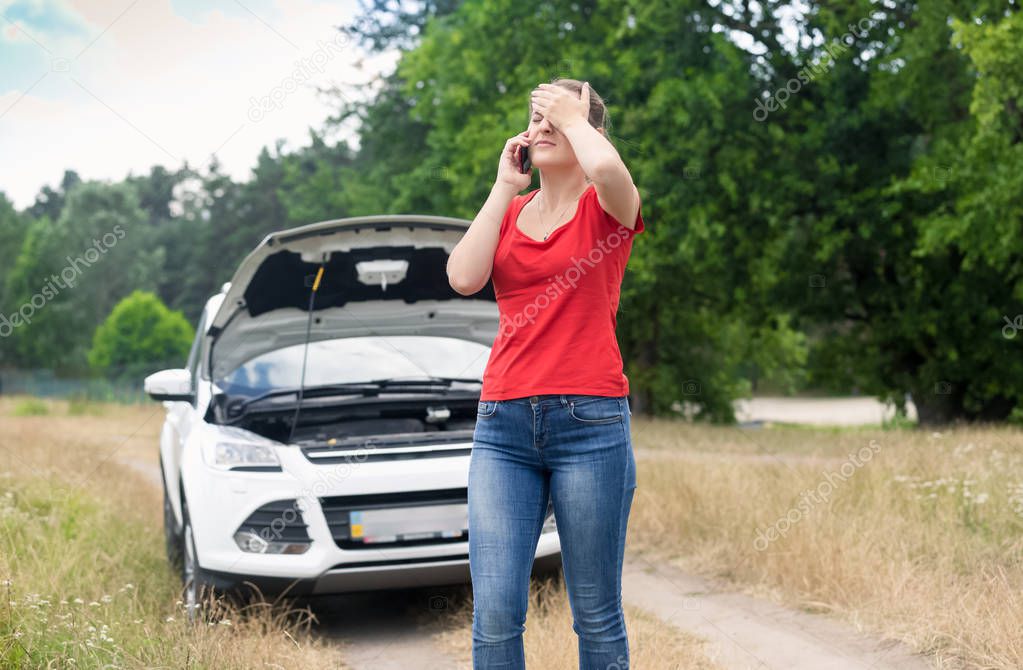 Stressed young woman with broken car on countryside road calling car service