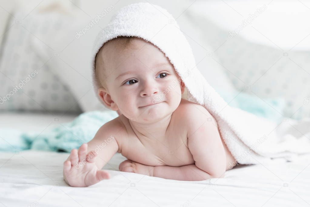 Cute 9 months old baby son lying under white towel on bed