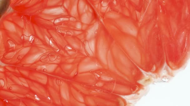 Macro 4k video of fresh grapefruit slice being squeezed and crushed on white background. Perfect abstract backdrop for organic food and healthy nutrition. Closeup of exploding fruit and flowing juice