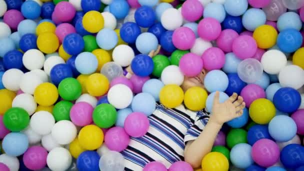 4k vídeo de feliz rindo criança menino deitado e dobrando na piscina cheia de bola de plástico colorido no playground no shopping — Vídeo de Stock