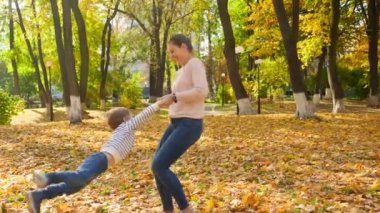 4k video, mutlu bir annenin küçük oğlunu ellerinin arasında tuttuğu ve onu sonbahar parkında döndürdüğü video.