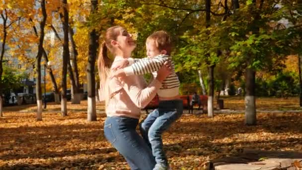 Vidéo 4k de joyeuse jeune mère riant caressant son petit fils après le saut et le filant dans le parc d'automne 