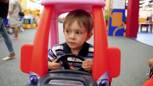 4k-Video von kleinen 4-jährigen Jungen, der in Tretauto auf Spielplatz in Einkaufszentrum reitet — Stockvideo