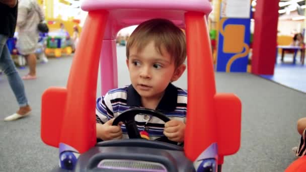 4k video of little 4 years old boy riding in pedal car on playground at shopping mall — Stock Video