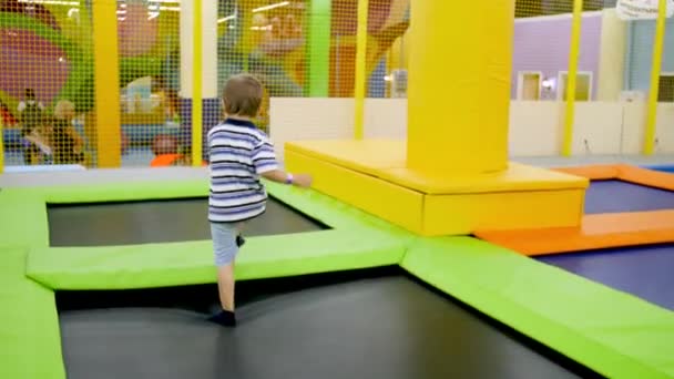 4k video de niño alegre corriendo y saltando en camas elásticas en parque de atracciones para niños en el centro comercial — Vídeo de stock