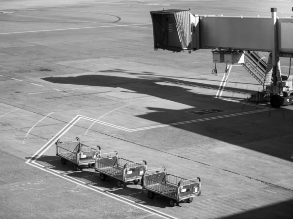 Black and white image of boarding gate corridor and empty carts for carrying and loading luggage in airplane — Stock Photo, Image