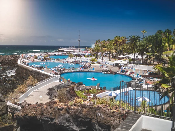 Beautiful image of people relaxing and having fun in swimming pools at hotel resort next to ocean beach — Stock Photo, Image