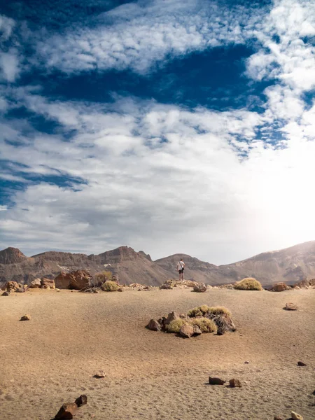 Schönes Bild eines jungen Mannes, der am Rande der Sandwüste steht und an heißen, sonnigen Tagen auf hohe Berge blickt — Stockfoto