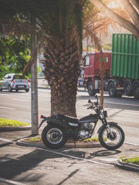 Gün batımında güzel palmiye ağacına giden yolda duran siyah motosikletin tonlu görüntüsü.
