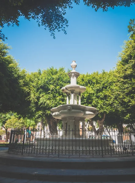 Toned image of white stone water fountain in the center of small square at european town — Stock Photo, Image