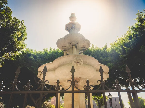 Toned image of beautiful decorated stone fountain against park trees and bright sun light — Stock Photo, Image