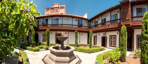 Panoramic image of stone water fountain in garden at inner court of old spanish house with wooden balconies — Stock Photo, Image