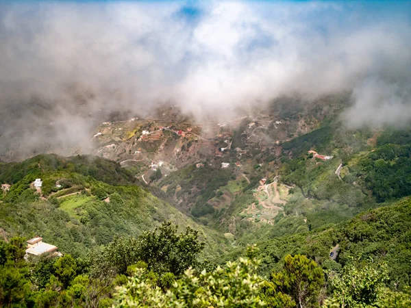 Vacker bild av moln som täcker liten by på den höga bergssluttningen överväxt med skog — Stockfoto