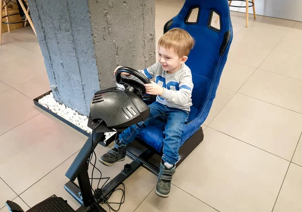 Bild eines fröhlich lachenden Kleinkindes, das auf dem Fahrersitz einer Spielkonsole sitzt, das Lenkrad hält und Videospiele spielt — Stockfoto