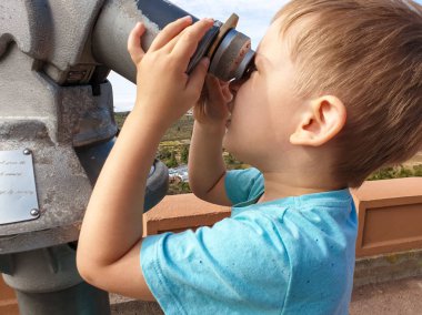 Dağın görüş noktasında madeni parayla çalışan dürbünle bakan küçük bir çocuğun yakın plan portresi.