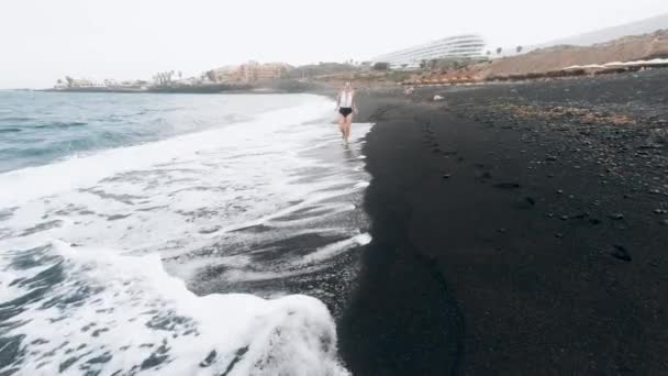 4k video of happy cheerful beautiful woman running on black volcanic ocean beach — Stock Video