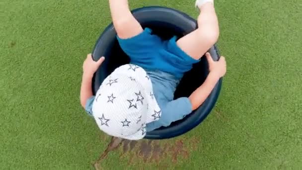 4k video de niño pequeño sentado en carrusel en el patio de recreo y girando rápido — Vídeo de stock