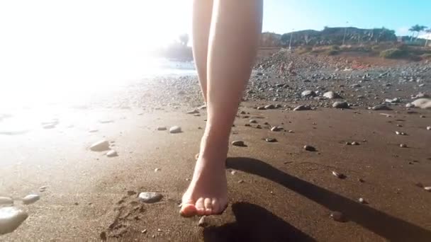 Primer plano 4k video de hermosos pies femeninos caminando sobre arena negra volcánica en la playa del océano al atardecer — Vídeos de Stock