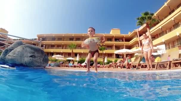 Видео медленного движения маленького мальчика с надувным кольцом, прыгающего в бассейне отеля — стоковое видео