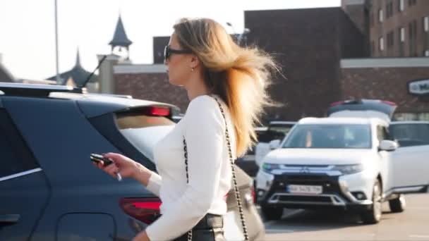 4k cámara lenta de vídeo de la joven hermosa mujer en falda caminando en el aparcamiento, abre su coche con llave y se sienta dentro — Vídeos de Stock