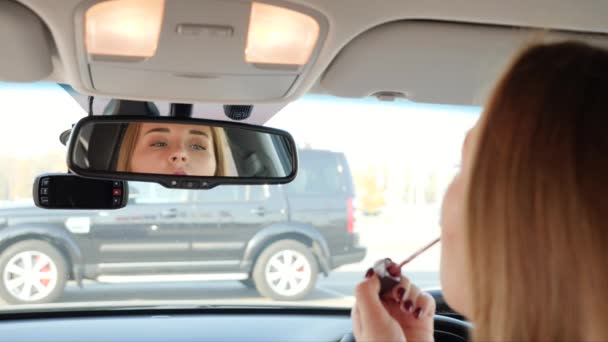 4k відео про молоду жінку, що сидить в машині і використовує дзеркало заднього виду, щоб використовувати губну помаду і грим. — стокове відео