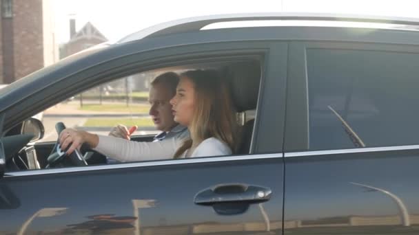 Erkek sürüş eğitmeninin arabada yolcu koltuğunda oturduğu ve sürücü kursunda kız öğrenciye yol gösterdiği 4k video. — Stok video