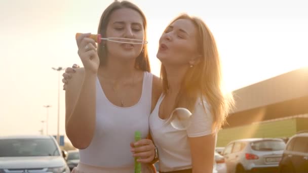 4k video en cámara lenta de dos chicas divirtiéndose juntas y soplando burbujas de jabón en la calle al atardecer — Vídeo de stock