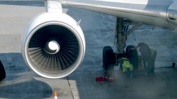 4k video of group of land crew in airport repairing chassis on passenger jet airplane. Aircraft wheel maintenance before flight — Stockvideo