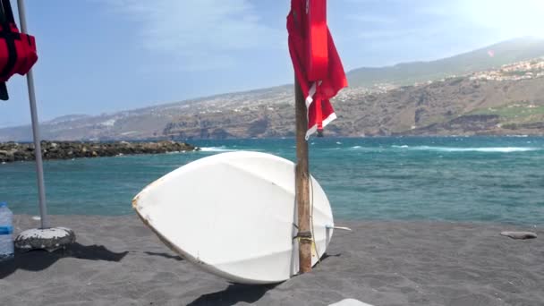 4k video av surfbräda ligger på tom strand med svart vulkanisk sand nära havet — Stockvideo