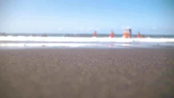 Primer plano fuera de foco video de la hermosa playa del océano con arena volcánica negra en el día ventoso soleado. Fondo tranquilo perfecto o telón de fondo para viajes o turismo — Vídeo de stock