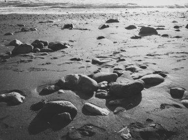 Gün batımında okyanus sahilinde çakıl taşları ve taşların siyah beyaz görüntüsü.